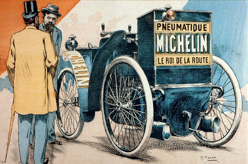 Gravure en couleurs représentant "L'Eclair". Plaquée à l'arrière du véhicule, une pancarte porte les inscriptions : "Pneumatique Michelin, le Roi de la Route". Deux hommes se trouvent à gauche de la voiture, dont Edouard Michelin. À l'arrière-plan de l'illustration, se déploient les couleurs Rouge, Blanc et Bleu, emblématiques de la république Française.